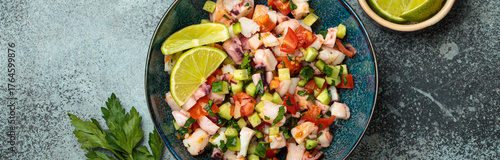 Fresh and vibrant peruvian seafood ceviche with shrimps, octopus, tomatoes, cucumber and parsley, served with lime in a bowl on a stone background from above, dish of Peru