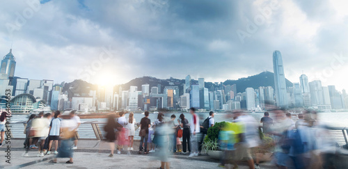 Tourists and citizens enjoying a cloudy day walking on the Hong Kong waterfront, with skyscrapers and victoria bay in the background