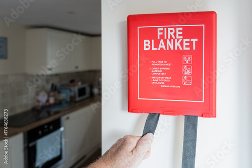 Newly installed Fire Blanket device seen being used for the first time by a home owner in a kitchen, due to a small fire whereby the flame will be smothered by the blanket.