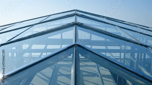 A geometric glass roof structure reflecting the sky with internal beams visible through the panels