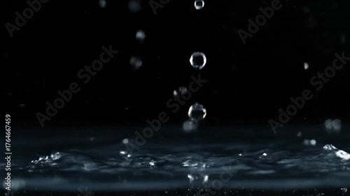 Water drops falling on a dark black background with bubbles and splashes