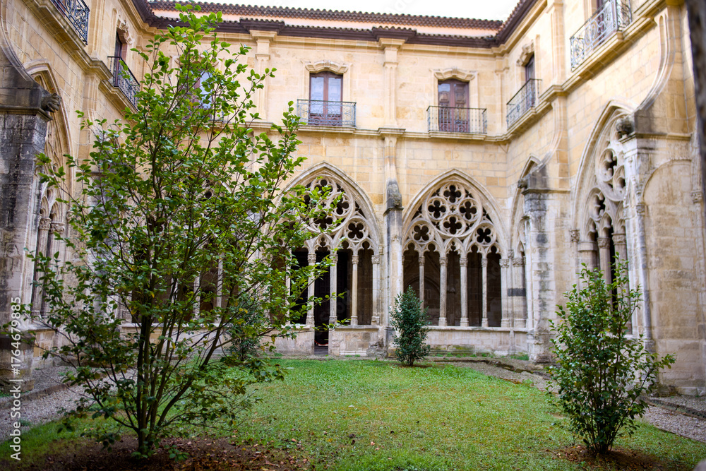 Fototapeta premium Medieval cloister garden with gothic arches and lush greenery in peaceful courtyard