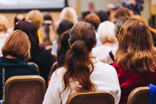 Female audience at the symposyum meeting, participants attendees in conference room hall listens to lecturer, group of women on a medical congress together listen to speaker on a stage at master-class