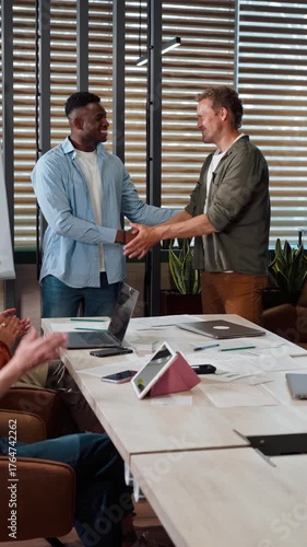 Confident successful diverse business partners smile and shake hands to the applause of colleagues