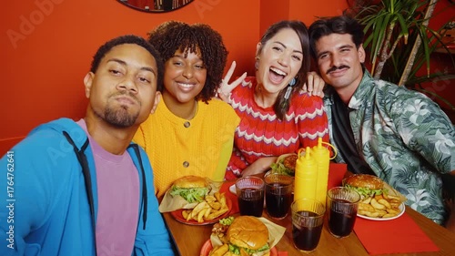 Multiethnic group of four happy friends sitting at a diner table, sharing a meal of burgers and fries while laughing and enjoying each other's company in a fun and vibrant atmosphere.