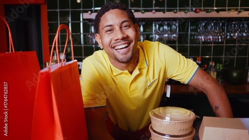 Smiling  waiter behind the bar counter handing a takeaway food order in paper bags and containers to a female customer in a modern and cozy restaurant setting