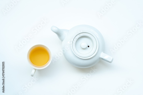 A top-down view of a white teacup filled with tea, placed next to a white teapot on a plain white background.