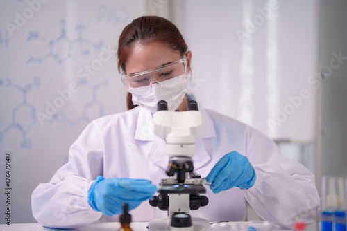 Asian adult woman scientist performs vital research observes samples microscope lab laboratory chemical formulas display experiment study