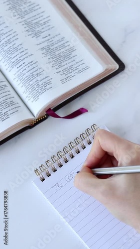 Human hand is writing inspirational biblical quote in a notebook with holy bible on the table. Vertical video. Christian study and education concept.