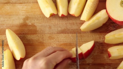 Hand is chopping apple slices on wooden cutting board. Top view.