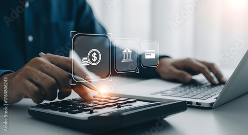 Person using a calculator and laptop with currency, bank, and credit card digital icons, analyzing finances and managing banking online.