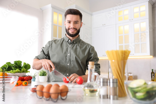 Wallpaper Mural Cooking process. Smiling man cutting tomato at table in kitchen Torontodigital.ca