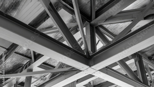 A black and white structural image of metal beams, intersecting at various angles, creating a roof framework