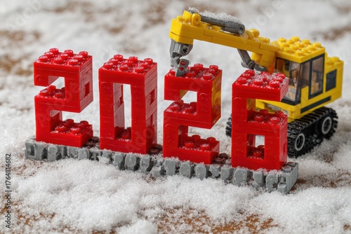 A yellow excavator lifts a red block while building a large 2026 sign in a snowy environment, showcasing creativity and fun during winter.