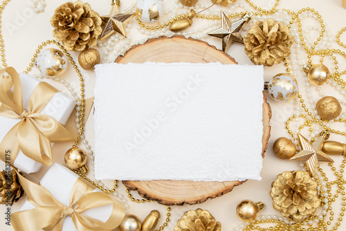 Handmade cotton paper card on wooden slice with golden Christmas and New Year decorations. Elegant flat lay with copy space for text or design.