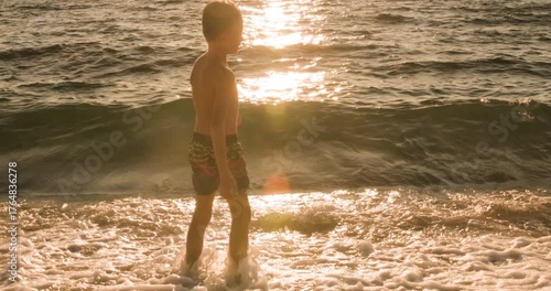 Young boy in silhouette enjoys throwing stones into the ocean at a beautiful sunset.