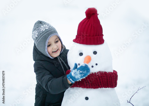 Cute little girl building snowman outdoor nature winter and playing with him. Children winter activity in Christmas time.