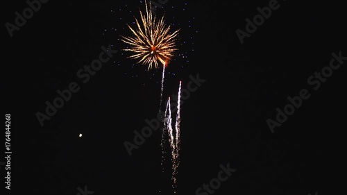 Bright fireworks explode in vibrant colors against the dark sky, creating a dazzling display during a community celebration. The atmosphere is filled with excitement and joy.