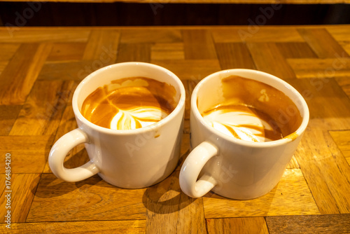 Hot latte, coffee with milk, and foam art on top in white ceramic cup on wooden table, in warm mood