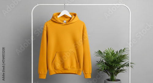Stylish mustard yellow pullover hoodie mockup hanging on a white rack against a gray background. Apparel template for showcasing clothing design