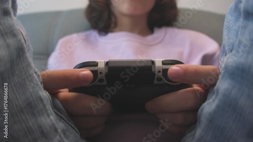 A boy plays on a game console. He holds a new gamepad. The gamer plays with the gamepad. The child sits on the couch and plays video games.