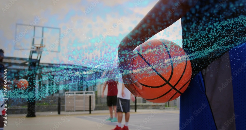 Fototapeta premium Athletic male player holding orange basketball and standing on urban court, with hoop and teammates