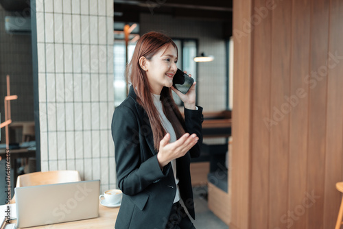 Young Asian businesswoman using mobile phone for a professional call, expressing confidence and connection in a modern office setup
