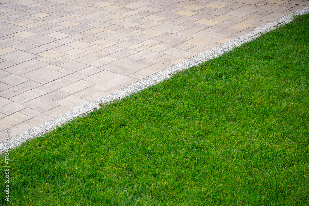 Naklejka premium Clean edge between paved walkway and vibrant green lawn. Diagonal. Real photo