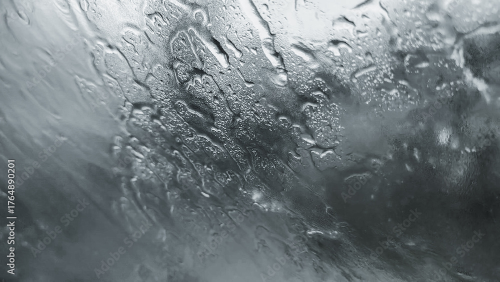 Fototapeta premium Raindrops on glass, creating a mesmerizing abstract pattern. The water droplets reflect light and distort the view, capturing a sense of both calm and movement.