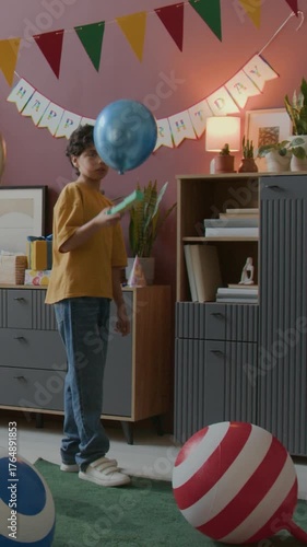 Vertical shot of little boys playing with colorful balloons in decorated for birthday party, children room