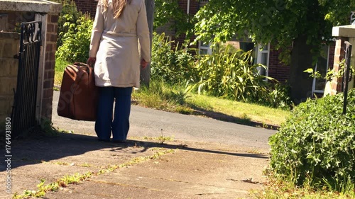 Woman carrying suitcase down driveway of home 