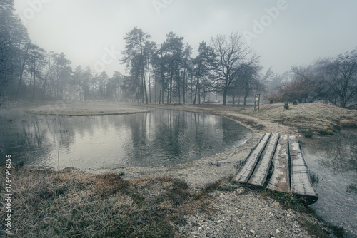 Misty forest lake with a wooden bridge in winter.
