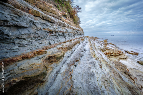 Layered rock formations meet the sea under a cloudy sky.