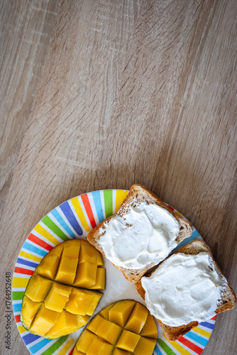 Delightful breakfast spread featuring creamy cream cheese toast and vibrant, ripe mango slices on a colorful striped plate, perfect for healthy eating inspiration.