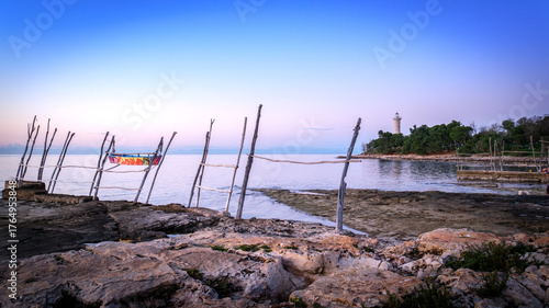 Colorful boat by wooden posts near lighthouse at sunset.