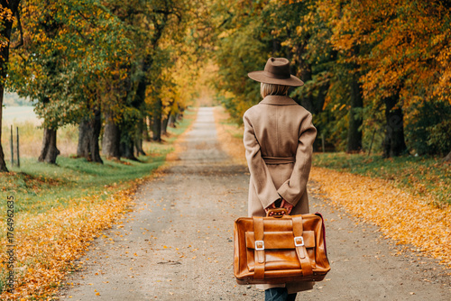 European woman in coat and hat walks along  yellow autumn trees