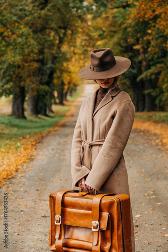 European woman in coat and hat walks along  yellow autumn trees