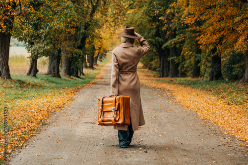 European woman in coat and hat walks along  yellow autumn trees
