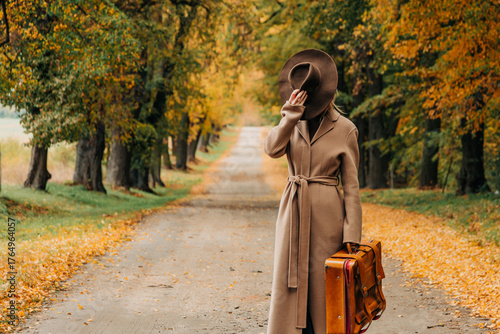 European woman in coat and hat walks along  yellow autumn trees
