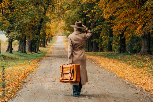 European woman in coat and hat walks along  yellow autumn trees