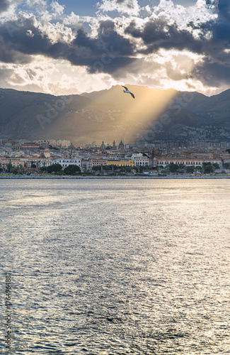 View of Palermo from the sea before sunset, southern Italy. The sunshine filter through the clouds, illuminating the cathedral and other historic buildings.
