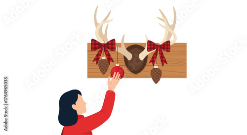 Woman's hand placing festive red ornament on rustic wooden mount with deer antlers and plaid bows, celebrating holiday spirit and cozy decor
