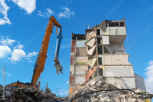 Building demolition with excavator. Powerful excavator demolishing old building under blue sky. Urban reconstruction, destruction, and industrial machinery concept.