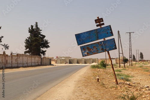 War-damaged old road sign reading Aleppo at the entrance of the Syrian city, full of bullet holes and rust. Reflects the impact of the Syrian Civil War, symbolizing destruction, and resilience. Syria