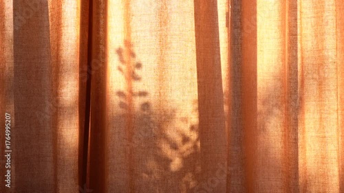 Golden hour sunlight streams through translucent orange curtains, casting soft shadows and creating a warm, inviting glow in an interior setting