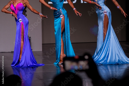 Contestants display stunning gowns in vibrant colors during a beauty pageant. The event takes place in the evening, capturing the grace and style of the participants.