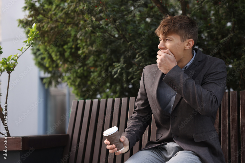 Obraz premium Young man with cup of drink suffering from nausea outdoors, space for text