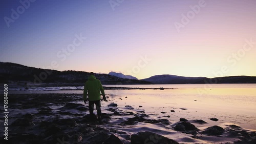Man in winter clothing walks thoughtfully across ice crusts on the shore of the Atlantic Ocean during an icy winter in Northern Norway near Tromso