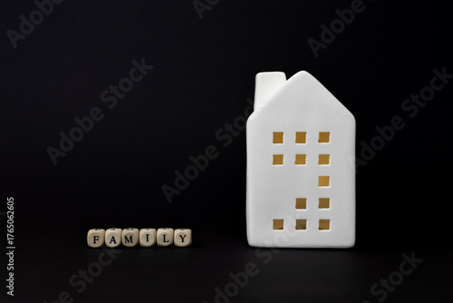 White ceramic house figurine with cut-out windows beside wooden blocks spelling family, representing home and family concept in modern design. copy space