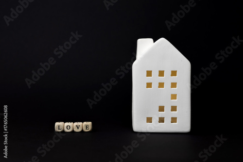 White ceramic house figurine with cut-out windows beside wooden blocks spelling love, symbolizing home and affection in a minimalist setting. copy space